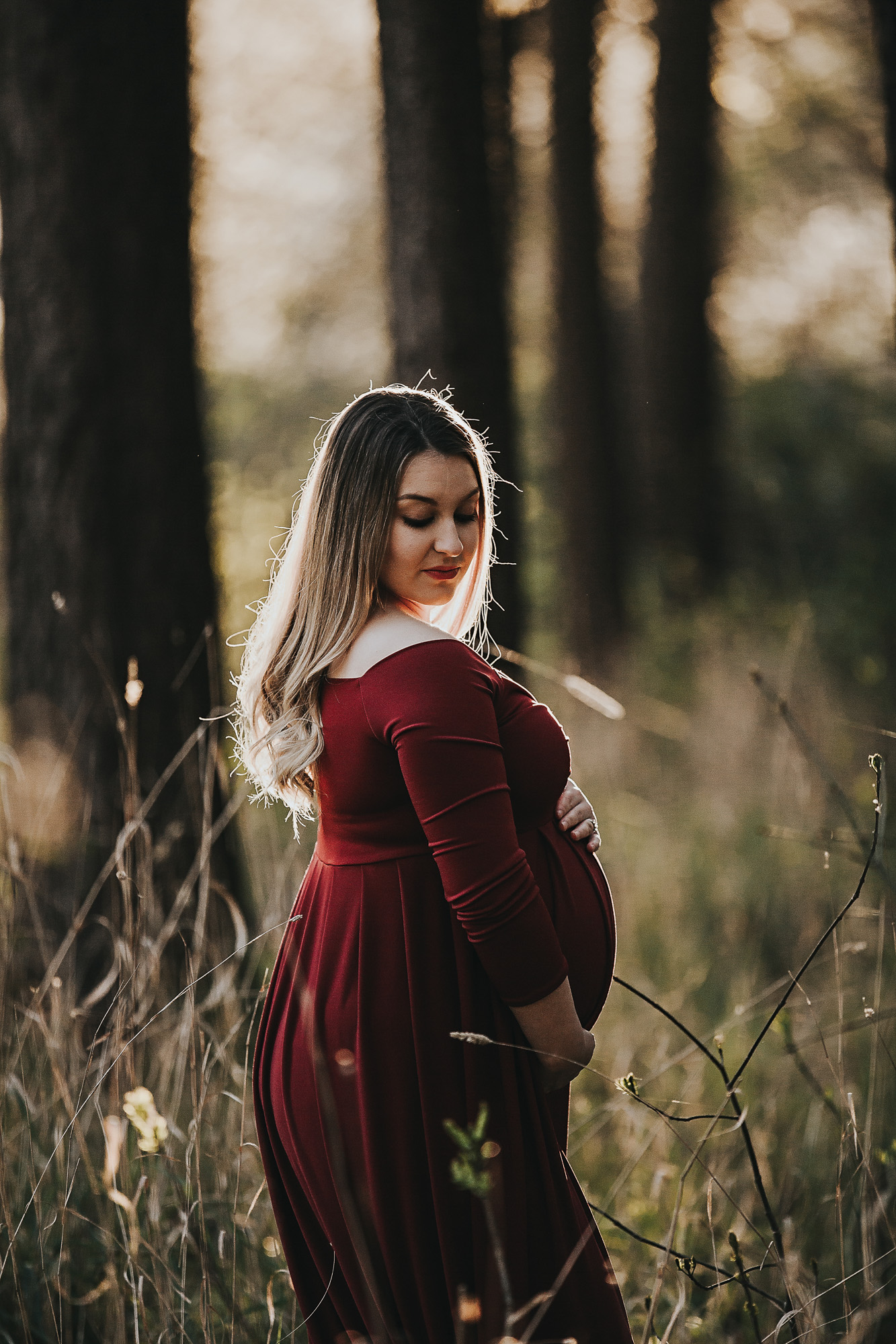 Adelaide maternity photographers photos of a pregnant woman in standing in a forrest in a red dress.