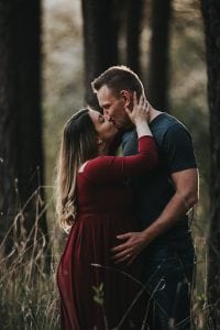 Adelaide maternity photographers photos of a pregnant woman in standing in a forrest in a red dress.