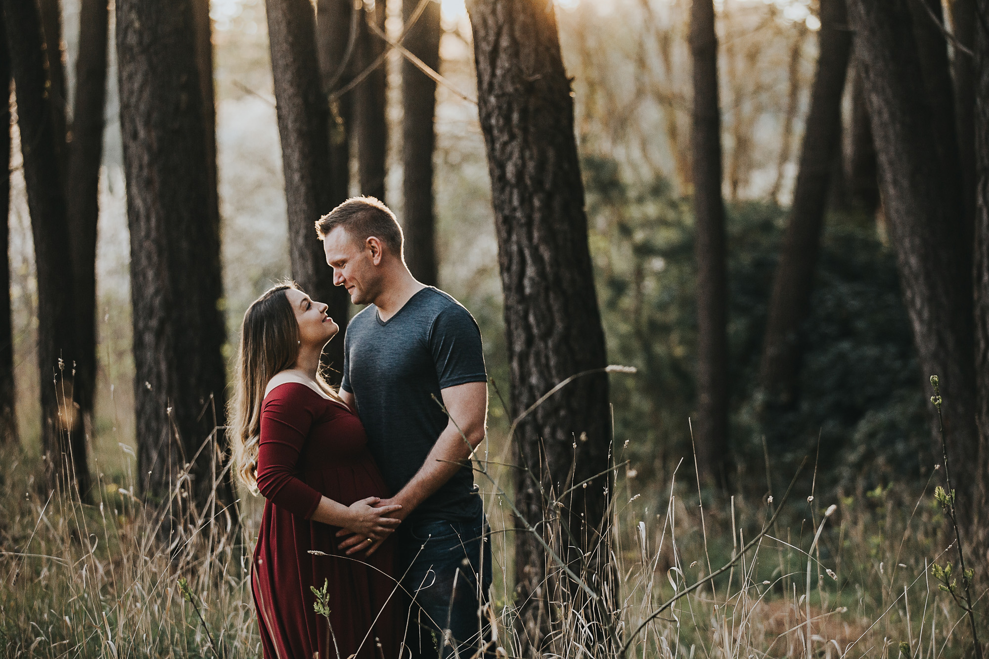 Adelaide maternity photographers photos of a pregnant woman in standing in a forrest in a red dress.