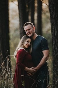 Adelaide maternity photographers photos of a pregnant woman in standing in a forrest in a red dress.