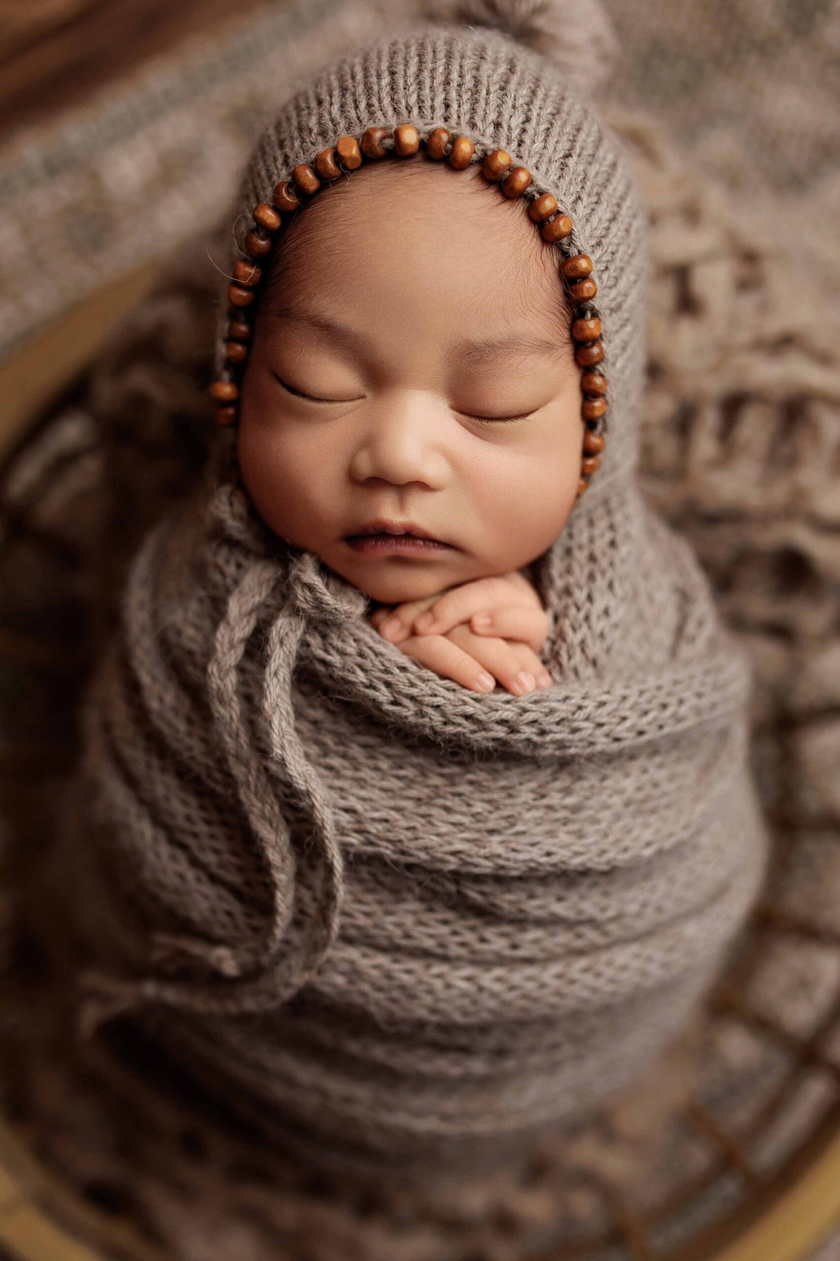 A close up of an Adelaide baby wrapped and wearing a bonnet asleep in a bowl.