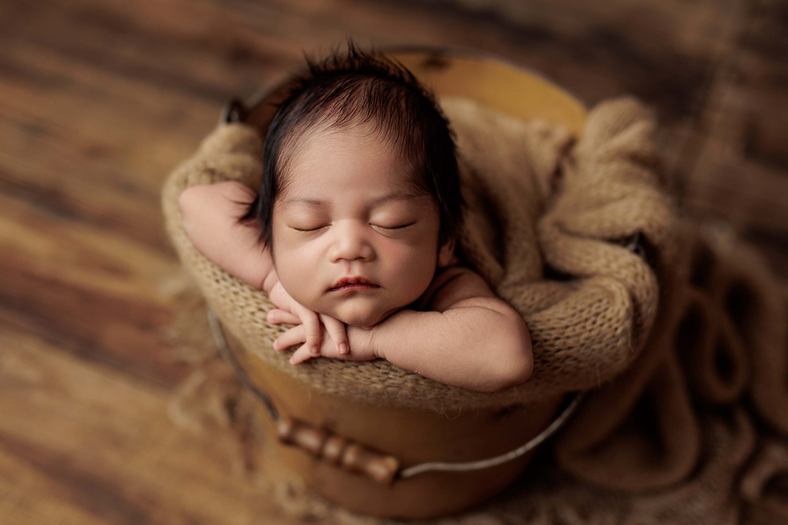 An Adelaide baby asleep in a tan bucket.