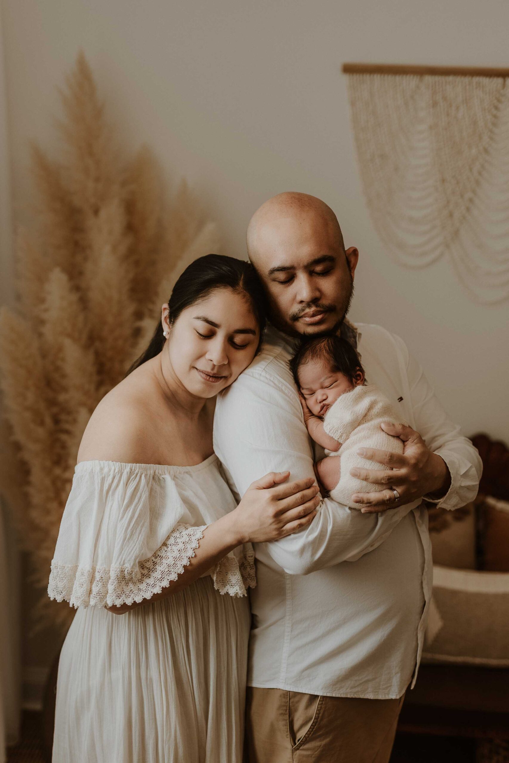 A couple in an Adelaide newborn photography studio hugging while holding their new baby.