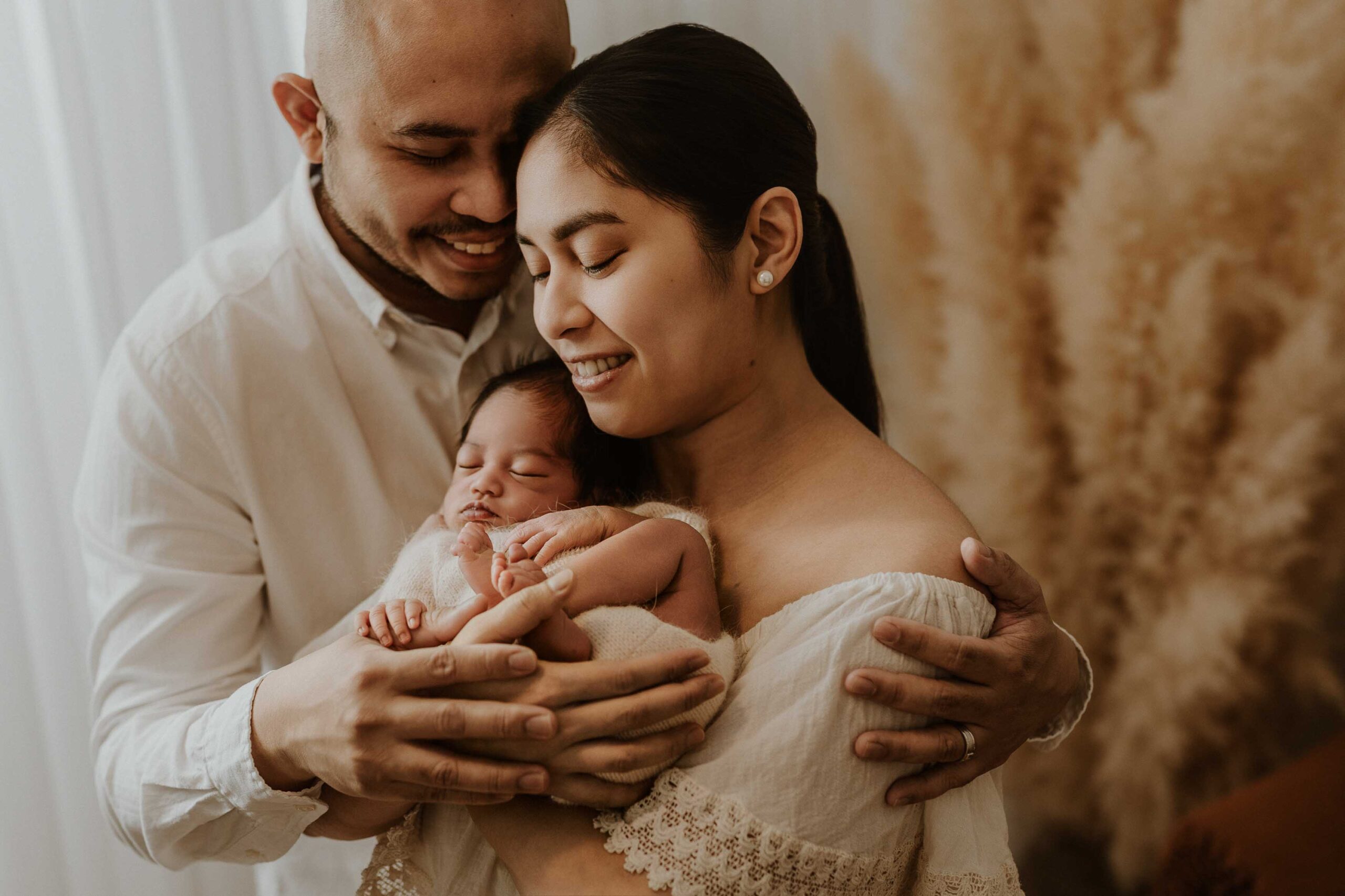 A closeup of a couple in an Adelaide newborn photography studio hugging while holding their new baby.