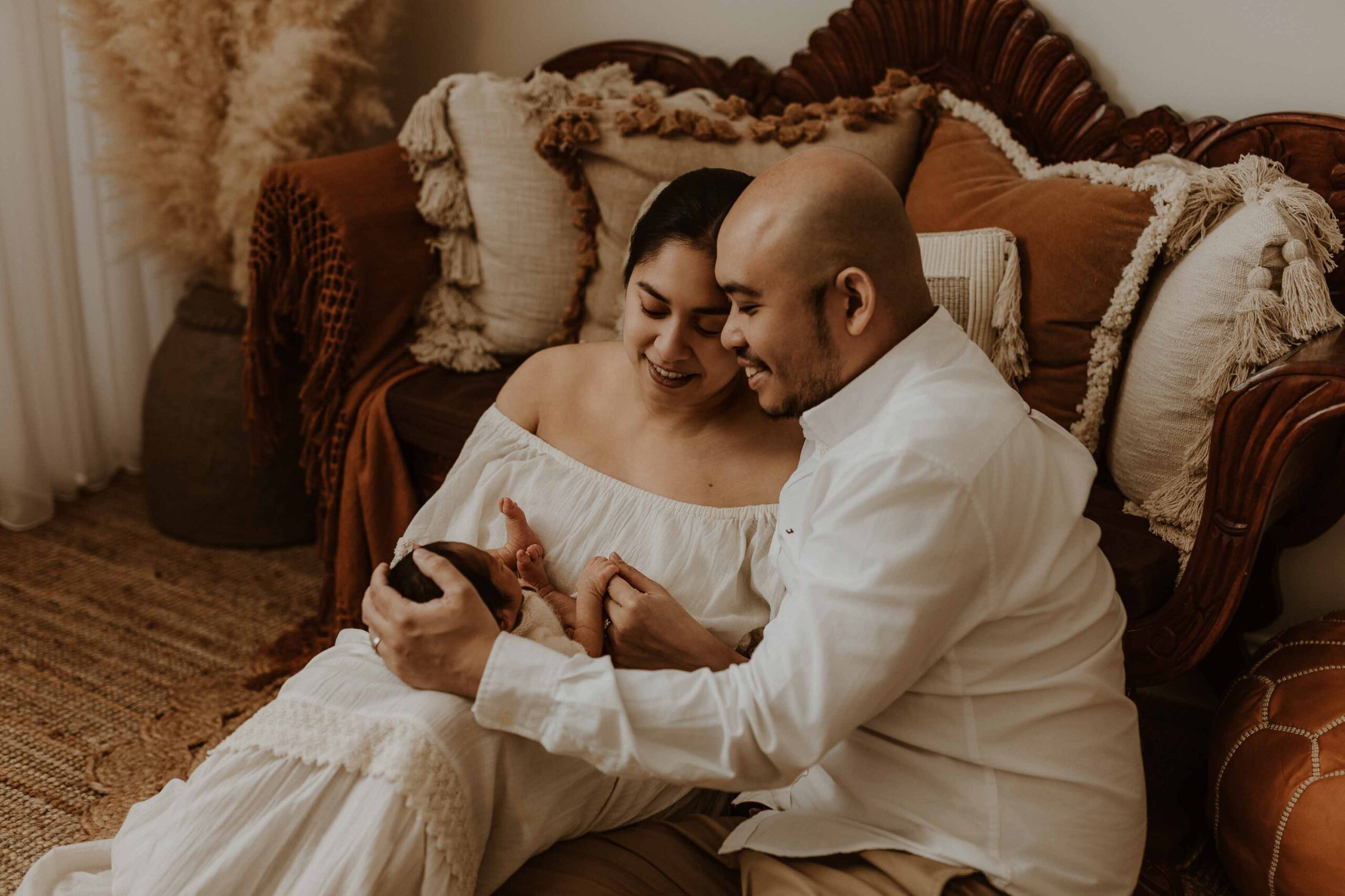 A couple in an Adelaide newborn photography studio sitting on the floor looking at their new baby.