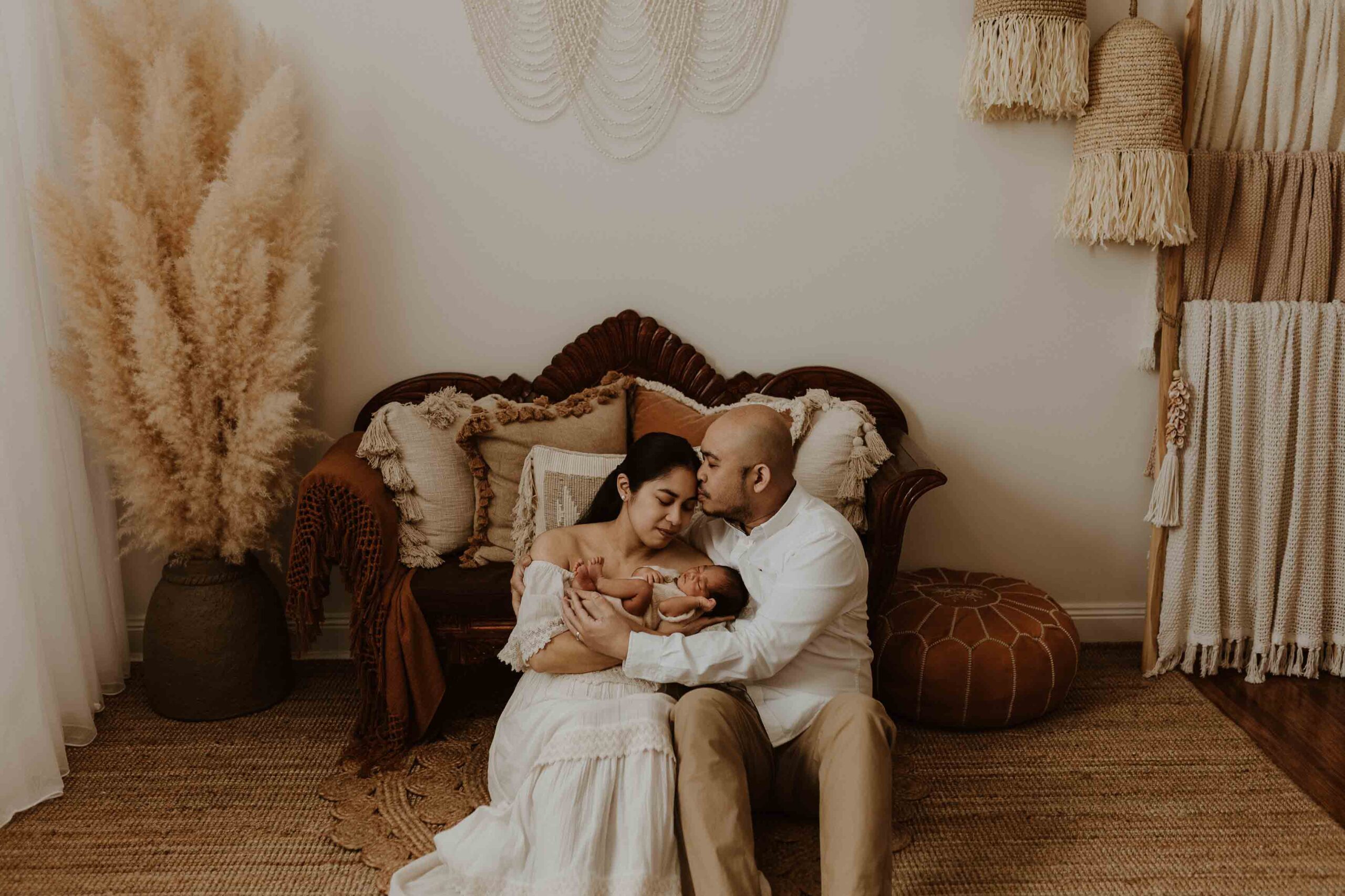 A couple in an Adelaide newborn photography studio sitting on the floor hugging each other while holding their new baby.